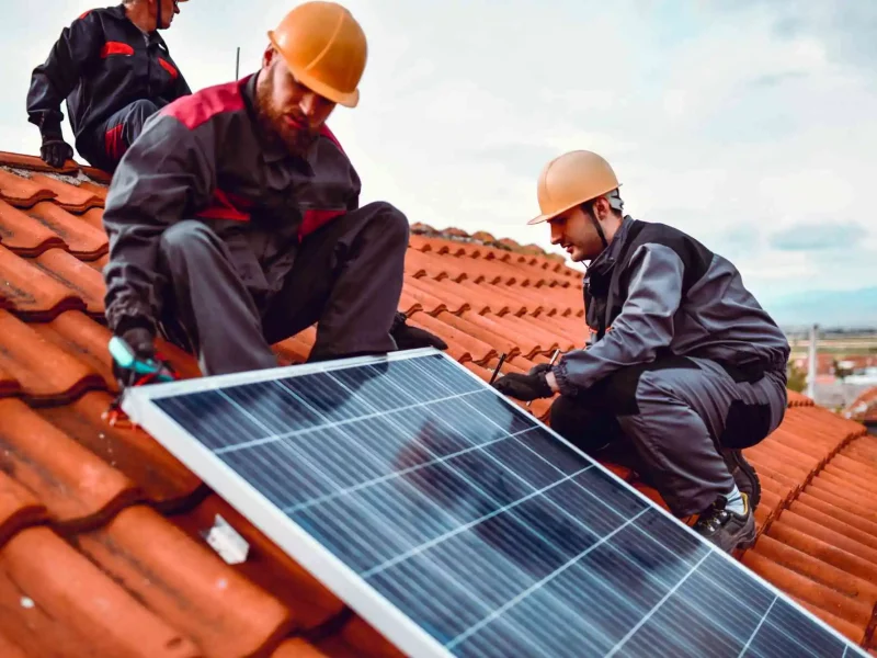 Dieses Bild zeigt Mitarbeiter einer Photovoltaik-Firma, die gerade ein Solarmodul auf einem Dach anbringen.